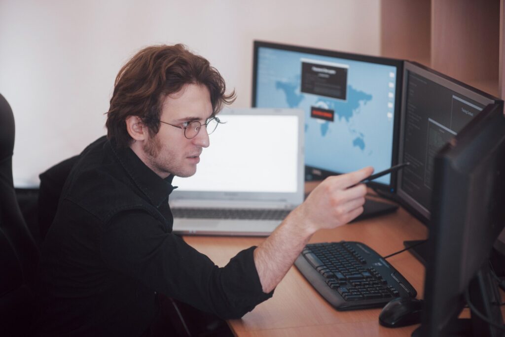 Mężczyzna programista pracujący na komputerze stacjonarnym z wieloma monitorami w biurze w firmie programistycznej. Technologie programowania i kodowania stron internetowych