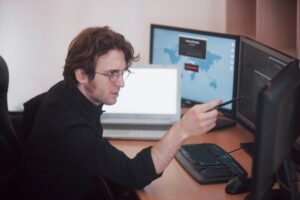 Mężczyzna programista pracujący na komputerze stacjonarnym z wieloma monitorami w biurze w firmie programistycznej. Technologie programowania i kodowania stron internetowych
