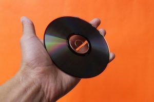 A hand holds up a cd against an orange background.
